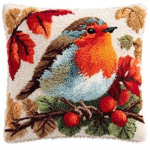 May include: A square, off-white throw pillow with a detailed, textured design of a robin bird. The bird has an orange breast, blue and brown wings, and is perched on a branch with red berries and green leaves. Autumn leaves in shades of red and brown surround the bird.
