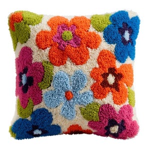Op de afbeelding: Een vierkant sierkussen met een getextureerd punch needle ontwerp van grote, veelkleurige bloemen. Het bloemmotief bevat levendige tinten oranje, roze, blauw en limoengroen op een gebroken witte achtergrond, wat zorgt voor een dicht, gelust oppervlak.