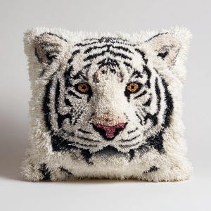 Könnte beinhalten: Ein quadratisches Zierkissen mit einem texturierten, getufteten Design eines weißen Tigergesichts. Der Tiger hat schwarze Streifen, leuchtend orangefarbene Augen und eine rosa Nase, die aus einem dichten, zotteligen Garnflor bestehen.