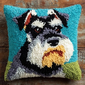 Peut inclure: Un coussin carré avec un motif en punch needle texturé représentant un chien Schnauzer. Le chien a un pelage noir, gris et blanc avec un museau jaune, sur un fond turquoise vif avec une petite zone d'herbe verte dans le bas du coussin.