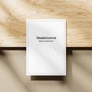 Könnte beinhalten: Ein weißer Gewohnheits- und Ziel-Tracker mit dem Titel "Mindful Growth" mit blauem Rand, der auf einer hellen Holzoberfläche liegt. Der Text ist in einer einfachen, modernen Schriftart gehalten. Der Hintergrund ist hellbeige mit Schatten.