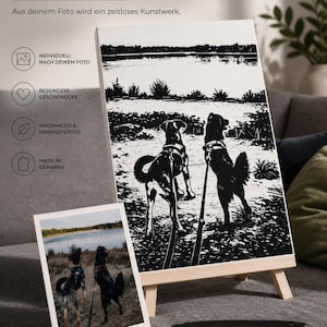 Könnte beinhalten: Ein schwarz-weißer Leinwanddruck auf einer Holzstaffelei mit einer Silhouetten-Illustration von zwei Hunden an der Leine an einem See, neben dem originalen Farbfoto. Text: DEINE LIEBLINGSMOMENTE FÜR IMMER FESTGEHALTEN und Einzigartig wie euer Moment. Zeitlos wie eure Bindung.