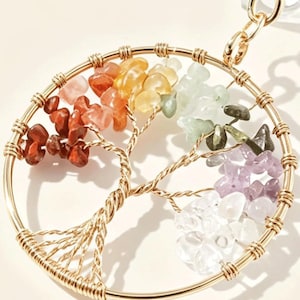 May include: A gold-colored metal tree of life pendant with a circular frame. The tree's branches are adorned with colorful gemstones, including red, orange, yellow, green, purple, and clear stones. A gold chain is attached.