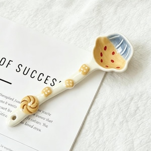 May include: A white ceramic mug with a black handle and the text "But First, Coffee" in a bold, black font. The mug is set against a blurred background, suggesting a cozy setting.