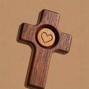May include: A wooden cross with a heart-shaped cutout in the center. The cross is made of dark brown wood, with a lighter wood heart inlay. The background is a solid, warm brown.