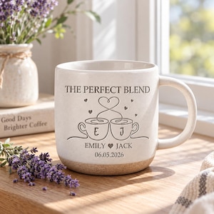 May include: A cream-colored ceramic mug with a speckled finish and a brown base. The front features the text THE PERFECT BLEND, a line-art graphic of two coffee cups with the letters E and J, the names EMILY and JACK with a heart, and 06.05.2026.