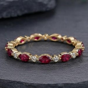 Könnte beinhalten: Ein goldener Eternity-Ring mit einem abwechselnden Muster aus marquise-geschliffenen roten Rubinen und rund geschliffenen weißen Diamanten. Der Ring besteht aus einer dünnen Metallschiene, die jeden Edelstein in einer Fassung hält.