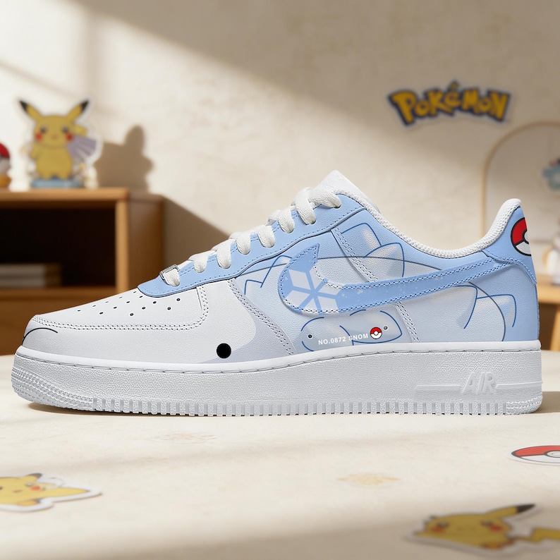 Pode incluir: T&ecirc;nis branco e azul claro com design de desenho animado. O t&ecirc;nis apresenta uma sola branca e um swoosh azul claro. O design inclui um personagem de desenho animado e a palavra "Pokemon".