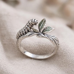 Puede incluir: Anillo de plata con una oruga detallada sobre una hoja. Las hojas tienen detalles de esmalte verde. La banda del anillo tiene un diseño orgánico y texturizado, creando una joya inspirada en la naturaleza.