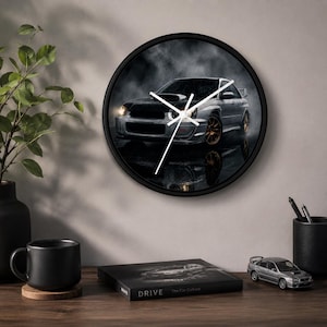 May include: A round wall clock with a black frame featuring a high-contrast image of a silver sports car with gold wheels on a dark, reflective surface. The clock face has simple white hour, minute, and second hands centered over the car graphic.