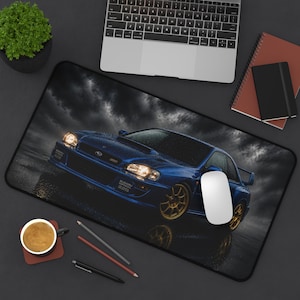 Pode incluir: Um tapete de secretária retangular com um carro Subaru Impreza 22B azul com jantes douradas, representado contra um fundo de céu escuro e tempestuoso. O carro é mostrado de um ângulo frontal de três quartos com os faróis acesos.