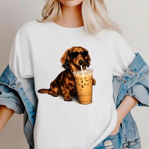 Peut inclure: T-shirt blanc avec un dessin d'un teckel marron portant des lunettes de soleil et tenant un caf&eacute; glac&eacute;. Le chien est repr&eacute;sent&eacute; dans une pose d&eacute;tendue, avec la tasse de caf&eacute; dans sa patte. Le graphisme est d&eacute;taill&eacute; et color&eacute;.