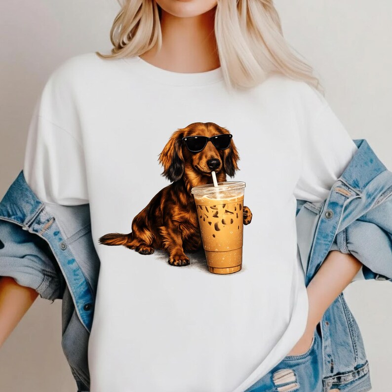 Peut inclure: T-shirt blanc avec un dessin d'un teckel marron portant des lunettes de soleil et tenant un caf&eacute; glac&eacute;. Le chien est repr&eacute;sent&eacute; dans une pose d&eacute;tendue, avec la tasse de caf&eacute; dans sa patte. Le graphisme est d&eacute;taill&eacute; et color&eacute;.