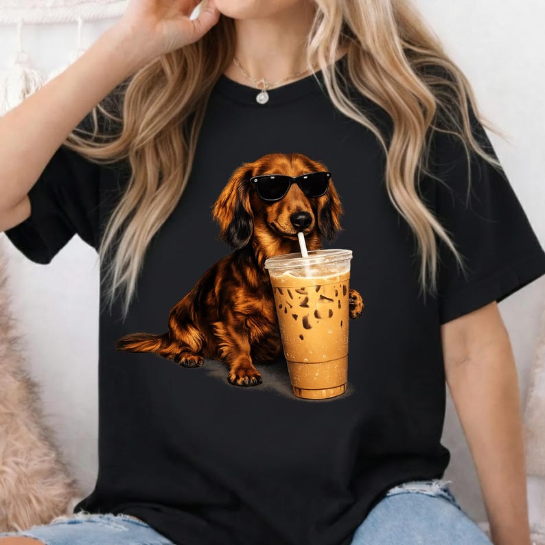 Peut inclure: T-shirt noir avec un dessin d'un teckel marron portant des lunettes de soleil et tenant un caf&eacute; glac&eacute;. Le chien a des poils d&eacute;taill&eacute;s et est dans une pose d&eacute;tendue, avec la tasse de caf&eacute; dans sa patte.
