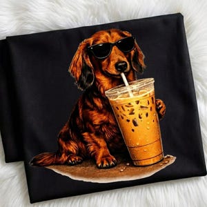 Peut inclure: T-shirt noir avec un motif de teckel portant des lunettes de soleil et buvant du caf&eacute; glac&eacute;. Le chien est brun avec des reflets noirs, tenant un gobelet en plastique transparent avec une paille.