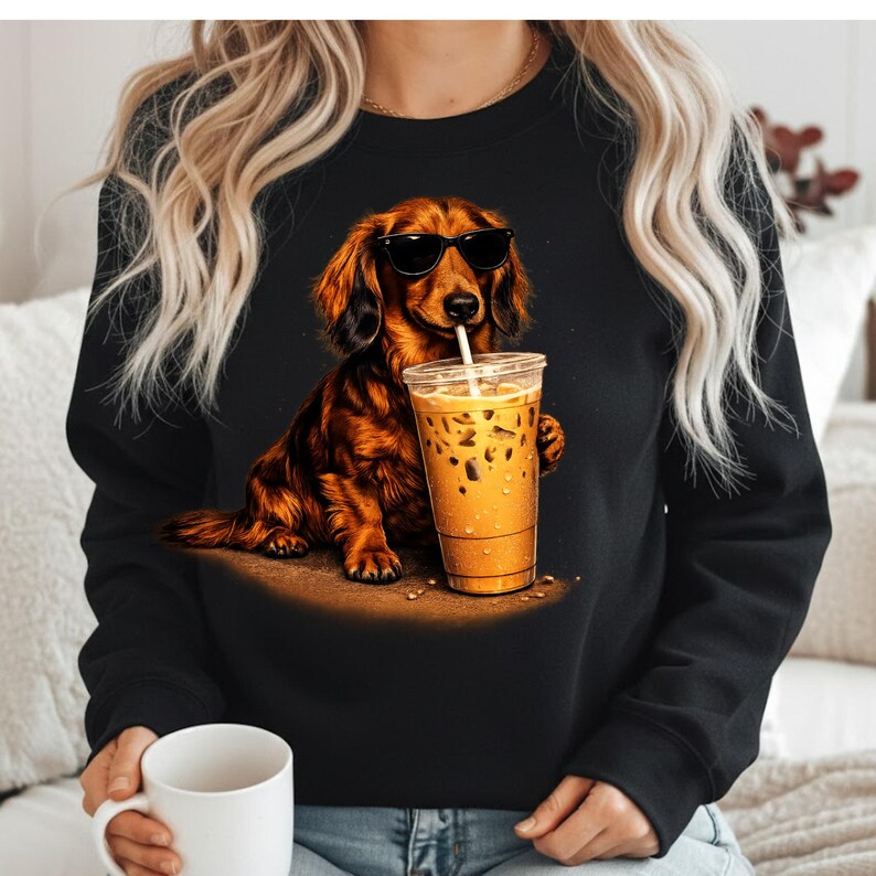 Peut inclure: Sweat-shirt noir avec un teckel marron portant des lunettes de soleil et buvant du caf&eacute; glac&eacute;. Le chien est le sujet principal, tenant un gobelet en plastique transparent rempli de caf&eacute; et de glace.