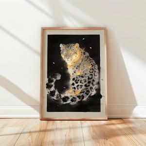 May include: Framed art print featuring a snow leopard with a black background. The leopard is depicted with a mix of white, black, and gold tones. The artwork is displayed in a wooden frame and leans against a white wall.