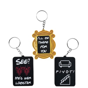 May include: Three keyrings with silver rings. One is a yellow frame with the text "I'LL BE THERE FOR YOU". Another is a black rectangle with red lobsters and the text "SEE? HE'S HER LOBSTER". The third is a black rectangle with a couch, stairs, and the text "PIVOT!"