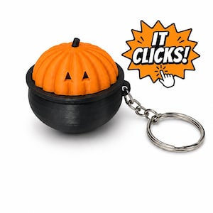 May include: A black cauldron-shaped keychain featuring an orange pumpkin lid with triangular eyes and a small stem. The pumpkin lid has a textured ribbed surface. A silver metal keyring is attached to the side. An orange starburst graphic with the text IT CLICKS! and a hand icon is positioned next to the keychain.