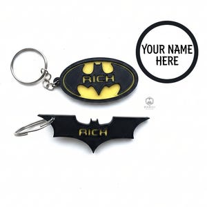 May include: Black and yellow Batman logo keyrings. One keyring is oval-shaped, the other is the bat symbol. Both have the word "RICH" in yellow. A circular graphic with the text "YOUR NAME HERE" is also present.