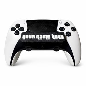 May include: White and black gaming controller with the text "your name here" in white. The controller has black buttons and a black centre section. The controller is designed for a gaming console.