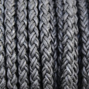 May include: Close-up of black braided leather cord. The cord is made of multiple strands of leather that are woven together to create a strong and durable cord.