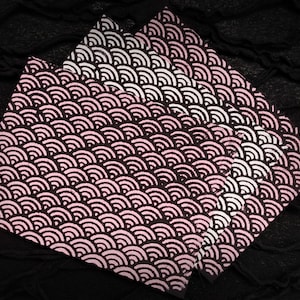 May include: Four square fabric napkins with a repeating pattern of pink and white curved lines on a dark brown background. The napkins are arranged in a layered fashion, with the pattern visible on each.
