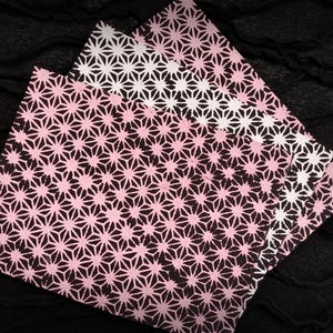May include: A stack of pink and white patterned paper napkins with a geometric starburst design. The napkins are arranged on a black, textured surface, creating a contrast between the colors and textures.