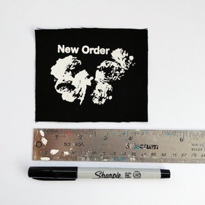 May include: Black fabric patch with white text that reads "New Order" and a white graphic design.