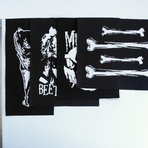 May include: Black fabric patches with white graphic designs. The patches feature illustrations of figures, the word "BEET", and bone shapes. A metal ruler with inch measurements is on the left.