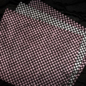 May include: Close-up of several sheets of paper with a repeating pattern of pink circles on a dark background. The pattern is arranged in a grid-like fashion, creating a textured appearance. The paper has a slight sheen.