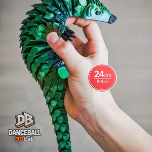 Pode incluir: Uma figura de pangolim articulada verde com textura de escamas em camadas, medindo 24 cm de comprimento. A figura apresenta um focinho pontiagudo, garras pretas e uma cauda longa. O logótipo da Danceball 3D Lab é visível no canto inferior esquerdo.