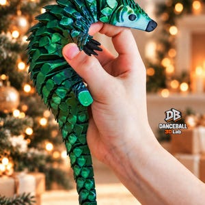 Op de afbeelding: Een 3D-geprinte, gearticuleerde pangolin-figuur met een metallic smaragdgroene afwerking en een lichtblauwe kop. Het figuur heeft een gesegmenteerd, flexibel lichaam en het logo DB DANCEBALL 3D Lab staat aan de zijkant.