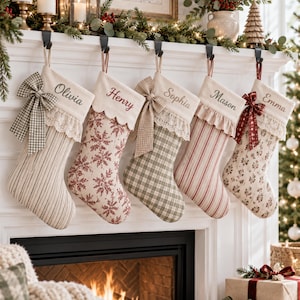 May include: Five personalized Christmas stockings hanging from a white mantel. Each stocking features unique fabric patterns including stripes, snowflakes, and plaid, accented with lace trim, bows, and embroidered names: Olivia, Henry, Sophia, Mason, and Emma.