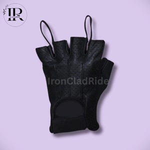 May include: Black fingerless glove with a perforated design. The glove has a wrist strap and loops for the middle and ring fingers. The text "IronCladRide" is visible on the glove. The background is a light purple color.