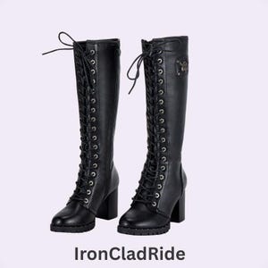 May include: A pair of black knee-high boots featuring a front lace-up design with silver-toned eyelets, a block heel, and a side zipper. The text IronCladRide is printed below the boots. The boots have a smooth finish and a rounded toe.