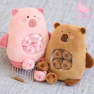 May include: Two plush bear toys, one pink and one brown, each with a pouch containing smaller bear-shaped plushies. The pink bear has a heart detail. Several small bear plushies are scattered around the toys.