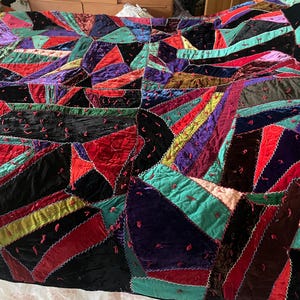May include: A colorful patchwork quilt with a geometric design. The quilt features a variety of jewel-toned velvet fabrics in shades of red, black, purple, teal, and gold. The pieces are sewn together with a decorative stitch.