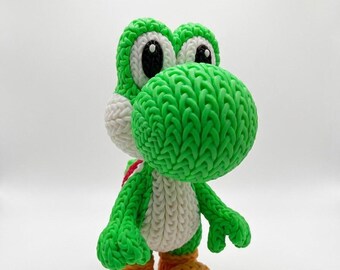 Può includere: Una statuina di Yoshi verde fatta a mano con dettagli bianchi, scarpe arancioni e una sella rossa. La figura ha grandi occhi espressivi ed è realizzata con un materiale intrecciato e strutturato. Il giocattolo è un personaggio della serie di videogiochi Super Mario.