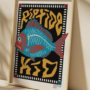 May include: A framed art print featuring a stylized fish illustration. The fish is teal with red accents, set against a black background with yellow text that reads "Riptide Kid." The print is in a light wood frame.