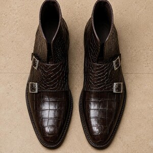 May include: A pair of brown leather ankle boots with a crocodile skin texture. The boots have a pointed toe and two silver buckles. The boots are approximately 6 inches tall.