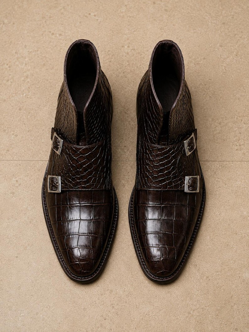 May include: A pair of brown leather ankle boots with a crocodile skin texture. The boots have a pointed toe and two silver buckles. The boots are approximately 6 inches tall.
