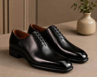Op de afbeelding: Een paar zwarte leren Oxford-schoenen. Deze formele schoenen hebben een gepolijste afwerking, een vierkante neus en zwarte veters. De hakken zijn ongeveer 2,5 cm hoog.