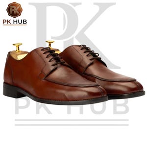 May include: A pair of brown leather dress shoes with black soles and laces. The shoes have a classic design with a rounded toe and are displayed with wooden shoe trees. The logo "PK HUB" is in the top left corner.