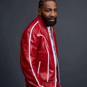 May include: A red track suit with white stripes. The jacket has a zip closure and the trousers have pockets. The outfit is made of a shiny material. The person is wearing a white shirt underneath the jacket.