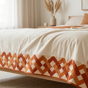 Peut inclure: Un couvre-lit de couleur cr&egrave;me dot&eacute; d'une large bordure orn&eacute;e d'un motif g&eacute;om&eacute;trique de losanges entrelac&eacute;s dans des tons orange br&ucirc;l&eacute; et terre cuite. La courtepointe est drap&eacute;e sur un cadre de lit en bois, avec un design cousu net.