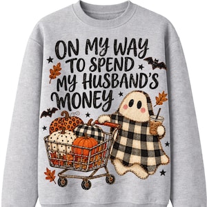May include: A light gray crewneck sweatshirt featuring a graphic of a ghost wearing a black and white buffalo plaid sheet, pushing a shopping cart filled with pumpkins, with the text ON MY WAY TO SPEND MY HUSBAND'S MONEY and small bats and leaves.