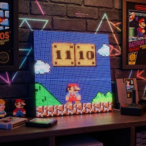 Puede incluir: Panel de luz LED pixelado que muestra una escena de Super Mario Bros. El panel muestra a Mario, colinas verdes y la puntuación 1110. Otros artículos de juegos retro están en el estante.