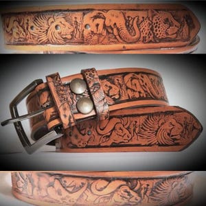 May include: A tan leather belt with intricate carvings of African animals, such as lions, elephants, and leopards. The belt has a silver buckle and two metal studs. The design features a safari theme.