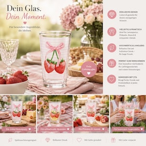 Könnte beinhalten: Ein klares Trinkglas mit einem Motiv aus zwei roten Erdbeeren, die mit einer hellrosa Schleife verbunden sind. Das Glas hat ein dezentes weißes Streifenmuster. Der Text auf dem Glas enthält die Phrase Dein Glas. Dein Moment.